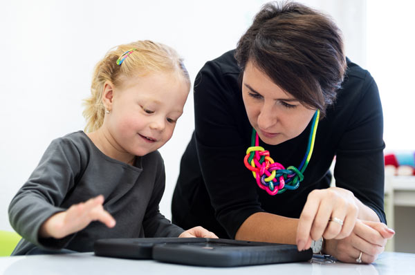 Woman observes little girl using tablet