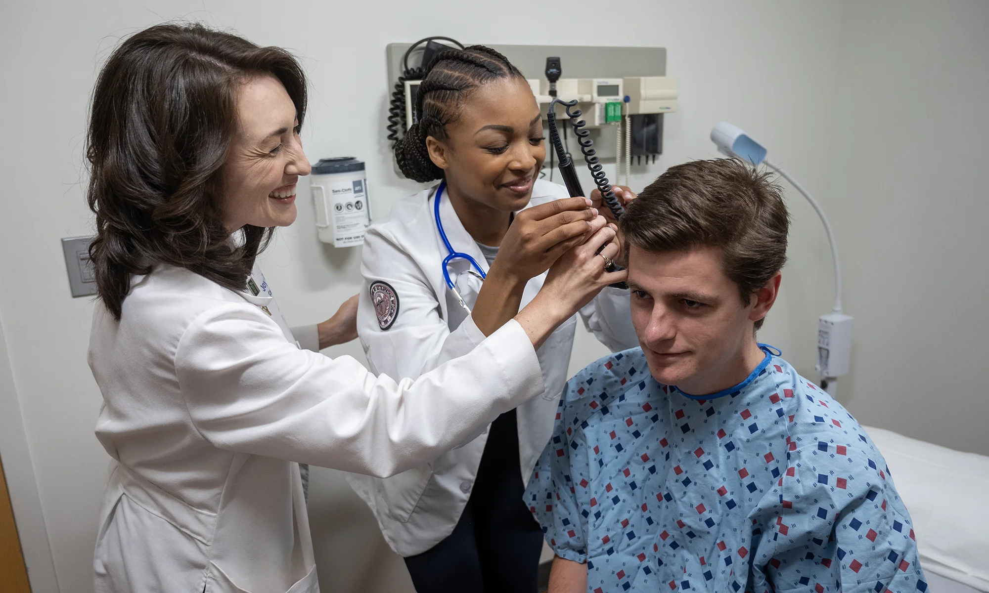PCOM medical students smile while examining a classmate posing as a patient during a hands-on learning exercise