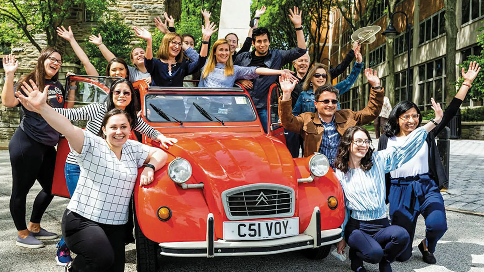 Graduate and medical students smile in front of a vintage car in front of PCOM's Philadelphia campus buildings