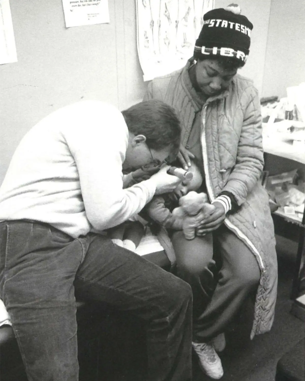 Black and white photo of a physician with PCOM's Family Medicine examining a young child on a mother's lap