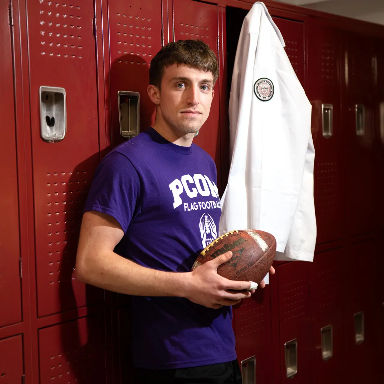 PCOM med student Adam Laudenslager (DO '25) holds a football in front of a locker