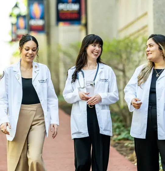 PCOM DO students smile and talk outside in their white coats.