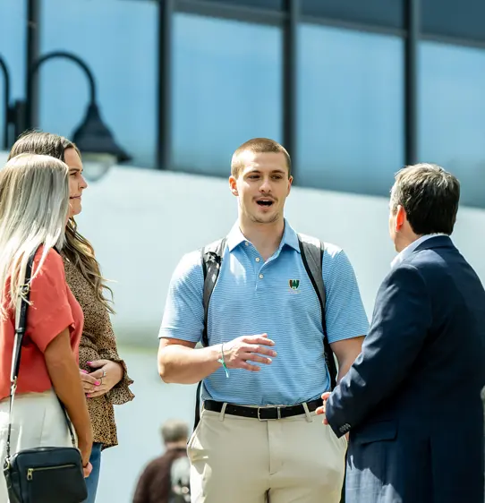 PCOM psychology students and faculty members smile as they talk outside on a campus pathway