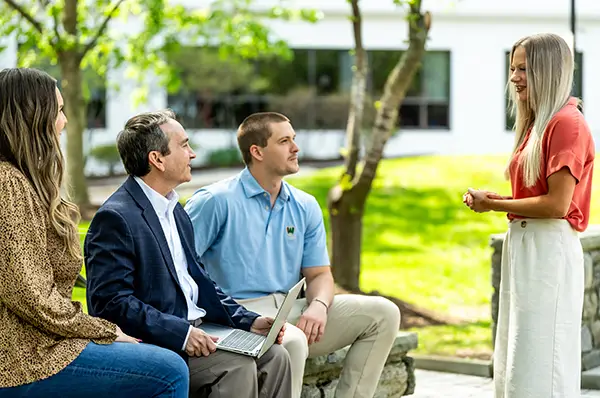 Three people sitting on a bench listen to a young woman.