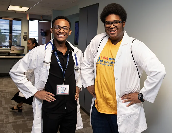 High school students smile while donning their student physician white coats in a lab PCOM's Opportunities Academy summer STEM program