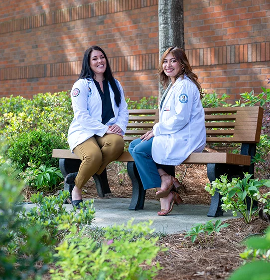 PCOM Georgia medical students smiling while sitting on a bench on PCOM Georgia's campus in Suwanee