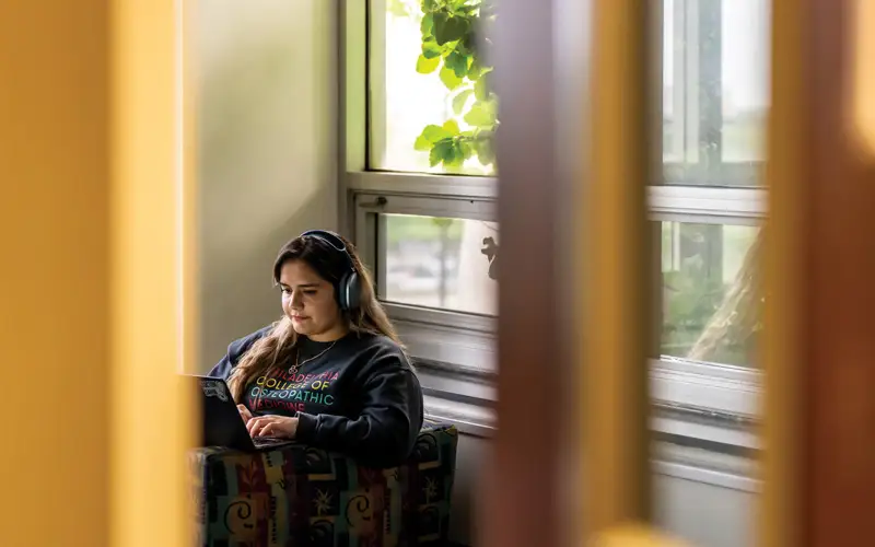 Golden hour bathes the O.J. Snyder Memorial Library in a warm glow, casting an interplay of light and shadow as a student studies diligently for an upcoming exam.