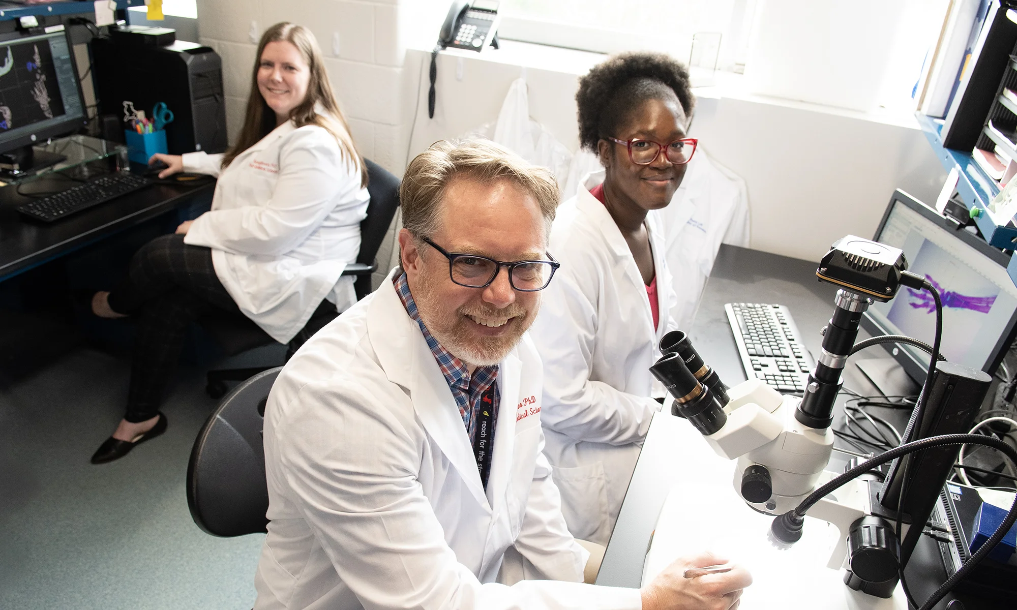 PCOM biomedical sciences students pursuing a concentration in research thesis smile alongside a faculty member in a laboratory