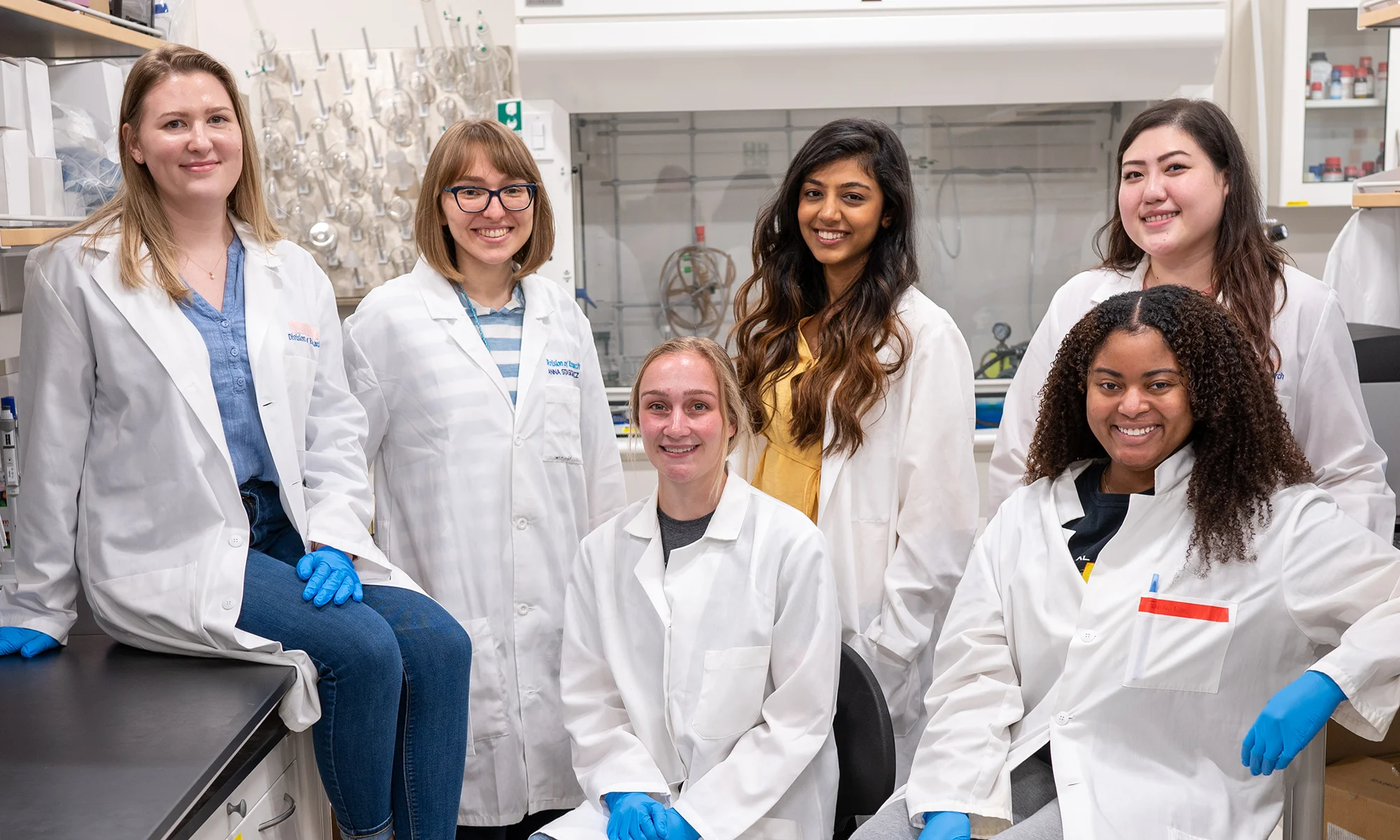 A group of PCOM students in research white coats smile in a PCOM Georgia research laboratory