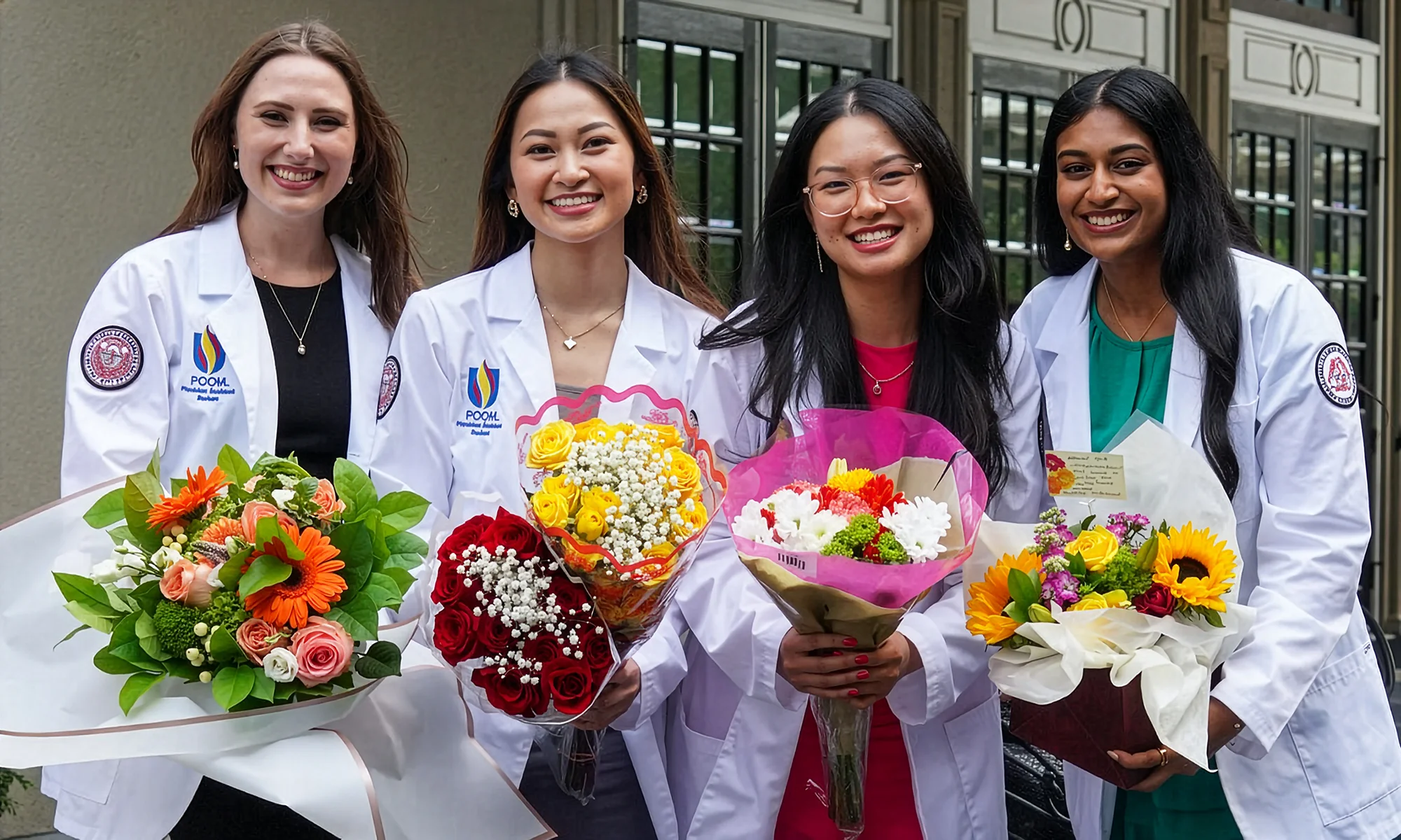 Four PCOM Georgia students smiling with flower bouquets after a white coat ceremony
