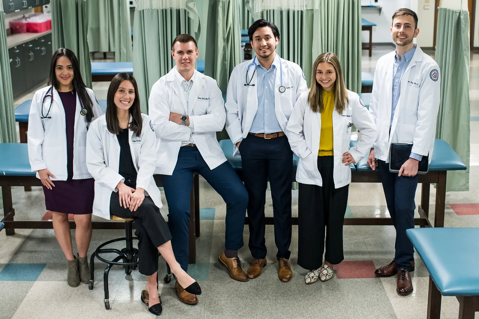 Physician assistant studies students smile in a group in a lab room at PCOM