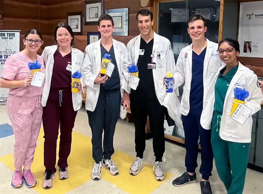 PCOM Georgia med student Ethan Lawson and his classmates smile in their white coats in the halls of Hillside Elementary in Roswell, GA