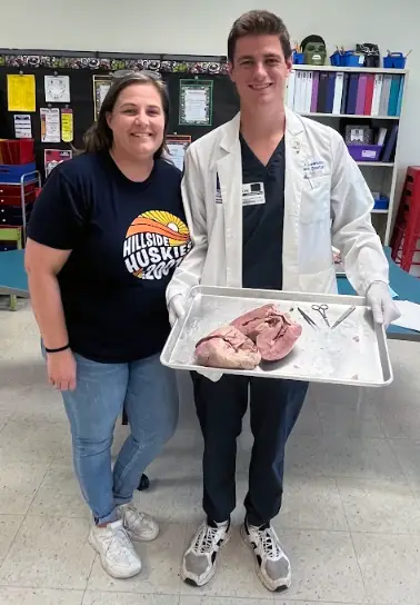 PCOM Georgia DO student Ethan Lawson smiles while holding a dissection tray alongside one of his former teachers during a volunteer event