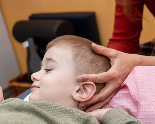 Young child lays on exam table while medical professional places hands on back of child's head