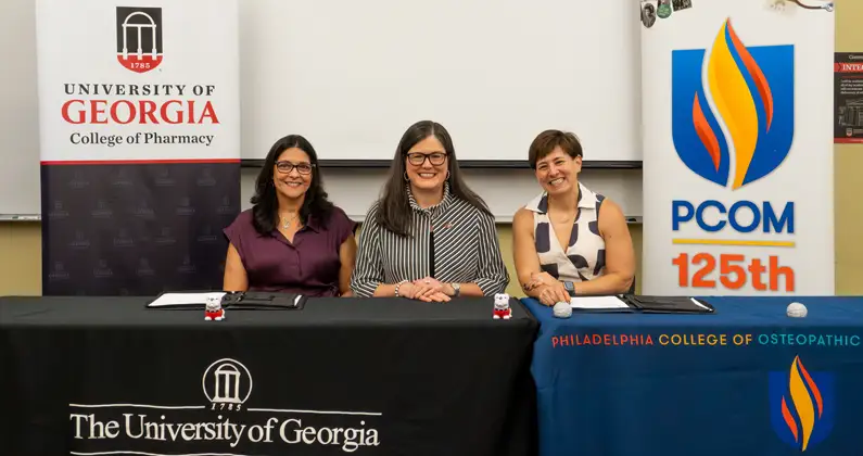 Marla Golden, DO ’88, Kelly Smith, PharmD, and Andrea Mann, DO, seated at table in front of UGA and PCOM banners