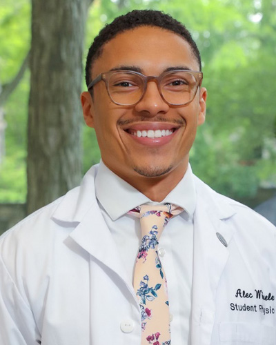 Professional headshot photograph of PCOM med student Alec Wheeler (DO '26), smiling in his white coat