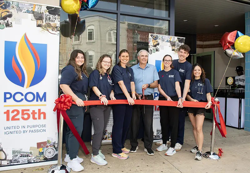 PCOM provost Kenneth Veit, DO, and medical students smile in front of PCOM signs and balloons as they cut a red ribbon at the Lancaster Avenue healthcare center