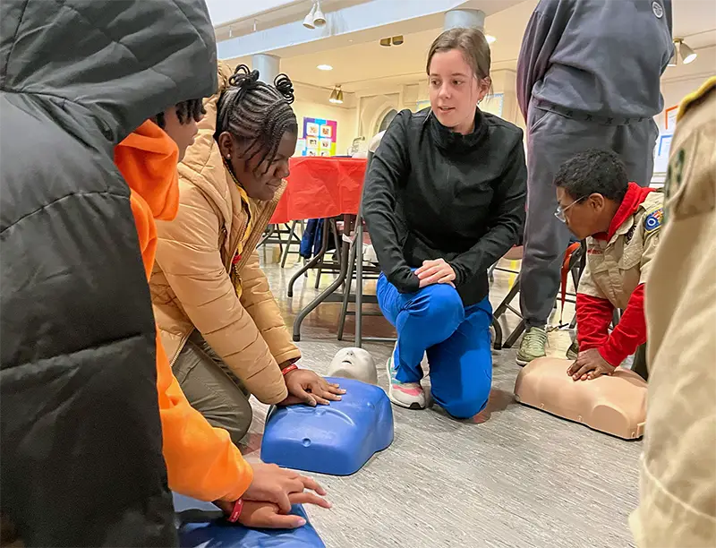 A PCOM med student helps boys and girls in the Scouts program learn how to do CPR with practice mannequins