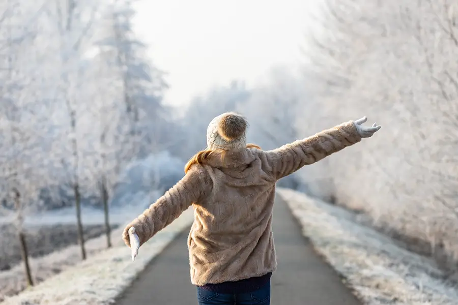 A person stretches and faces the sun on a frost-covered winter trail in order to improve their mindfulness and mental health during winter