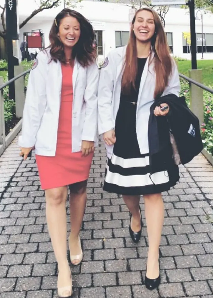 PCOM's Christina Monaco Poloni and a friend laugh as they walk on PCOM's campus in their student physician white coats.
