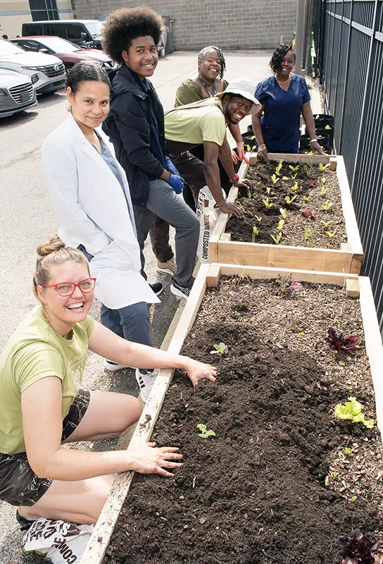 PCOM staff members and Philadelphia activists smile as they plant seedlings at a community garden in the Lancaster neighborhood of Philadelphia.