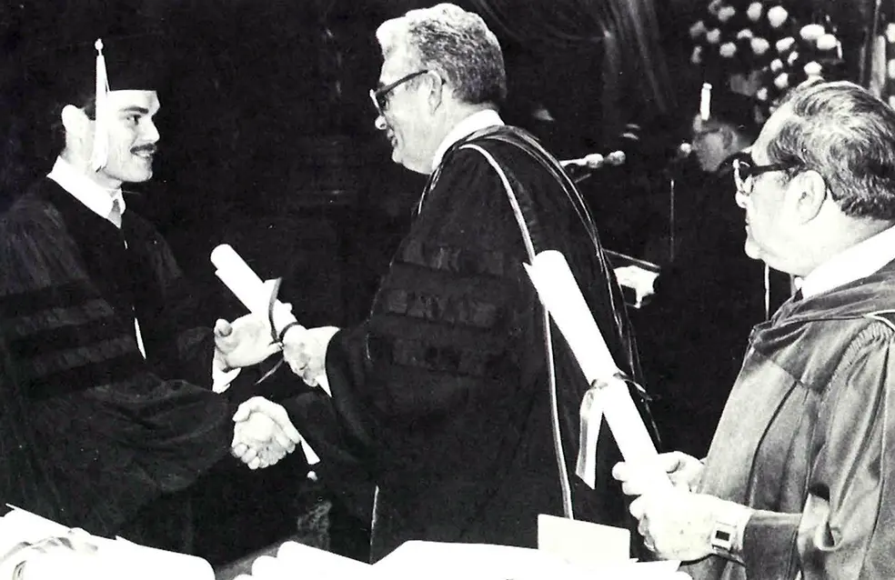 Black and white photo of PCOM's 1982 Commencement ceremony with Dr. Everett receiving his diploma from Dr. Rowland.
