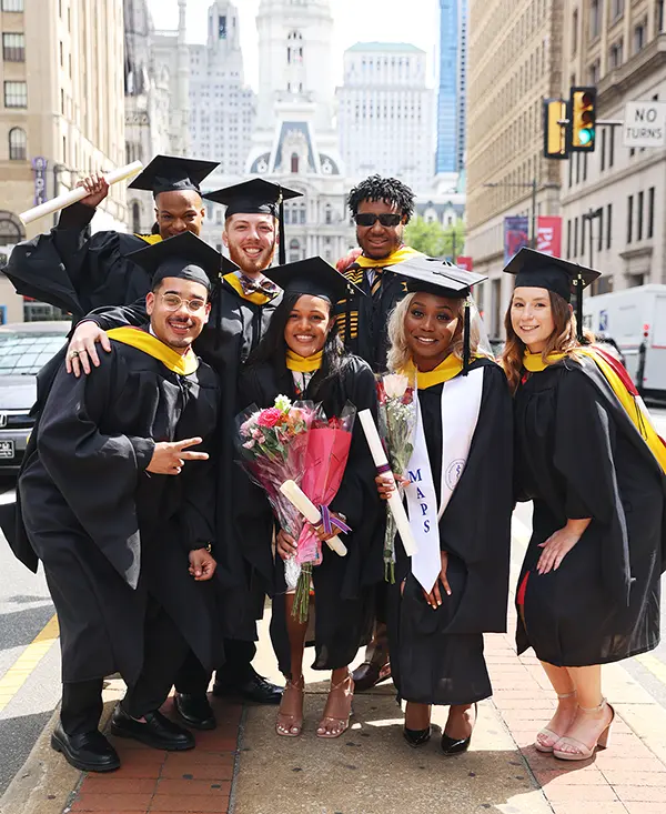 PCOM grad students smile in their caps and gowns on Broad Street in Philadelphia, PA