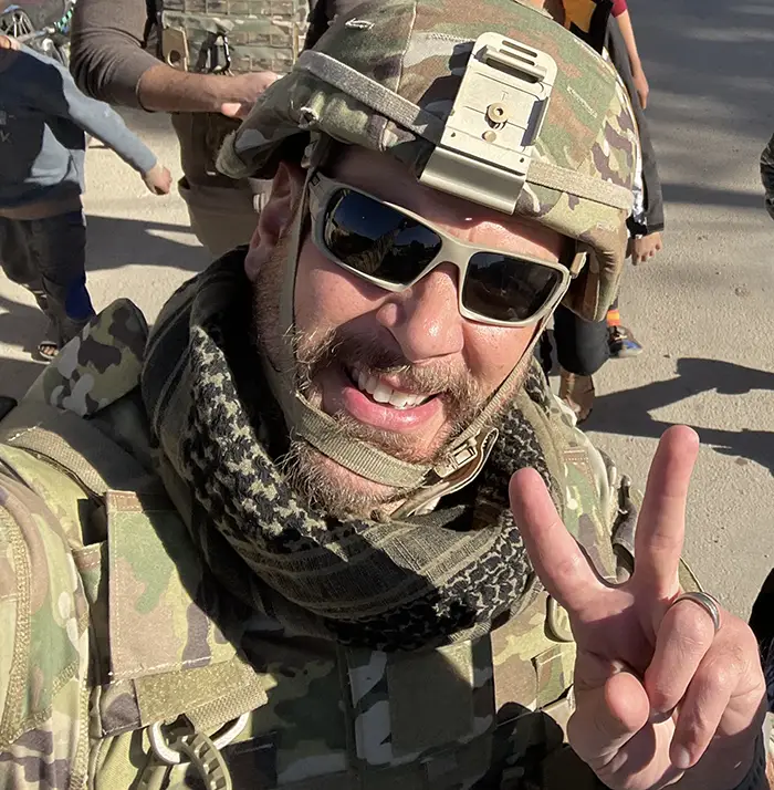 Robert Bassett, DO '06, wears sunglasses and Army camoflauge gear while walking on a street in Syria during his deployment