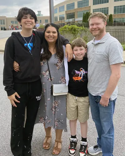 PCOM's Maricela Montijo-Davis smiles with her family outside of a school building