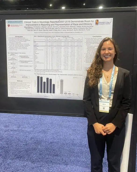 PCOM DO student Maya Rakoczy smiles in front of her research poster titled "Clinical Trials in Neurology Registered 2007-2018 Demonstrate Room for Improvement in Reporting and Representation of Race and Ethnicity"