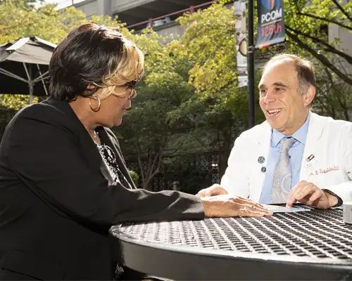 Arlene and Dr. Finkelstein sit together at a patio table on the PCOM Philadelphia campus.