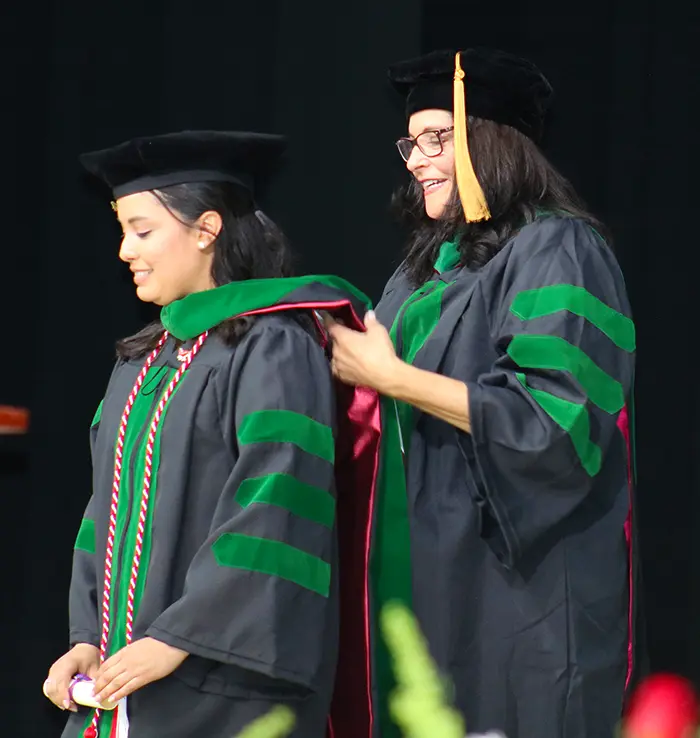 A PCOM South Georgia graduate smiles as she is hooded by the dean during the commencement ceremony