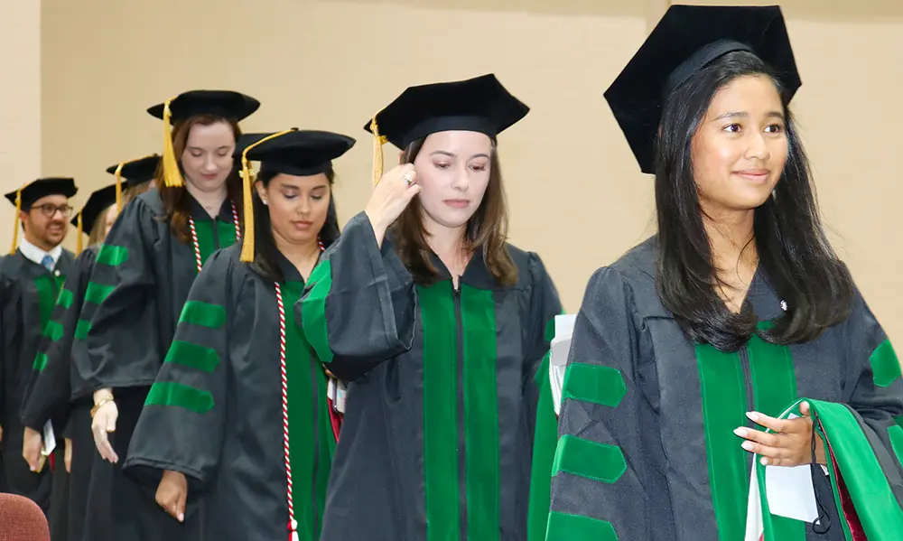 A row of PCOM South Georgia DO graduate smile as they walk in their caps and gowns.