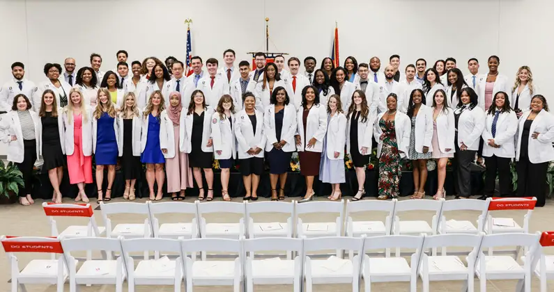 DO students stand on stage in white coats