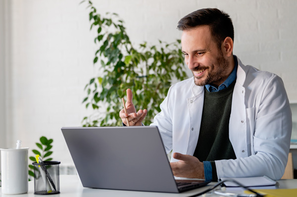 Physician smiles as he attends PCOM's geriatric medicine CME course using his laptop