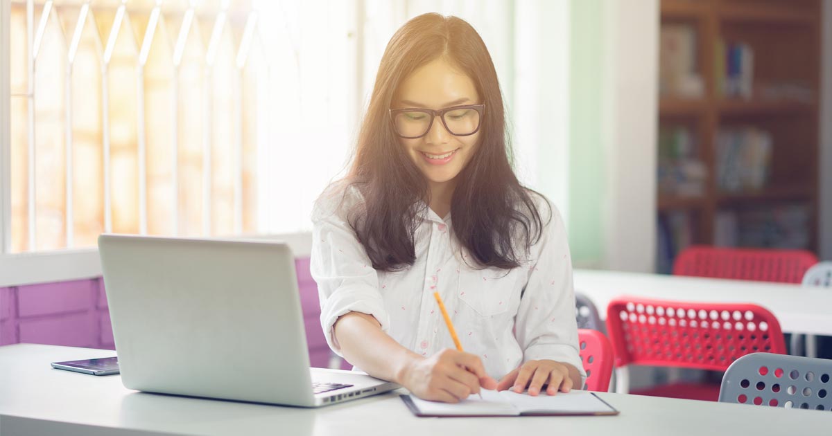 A first-generation college student smiles as she uses a laptop to attend PCOM South Georgia's virtual info session on admissions for first-gen medical students