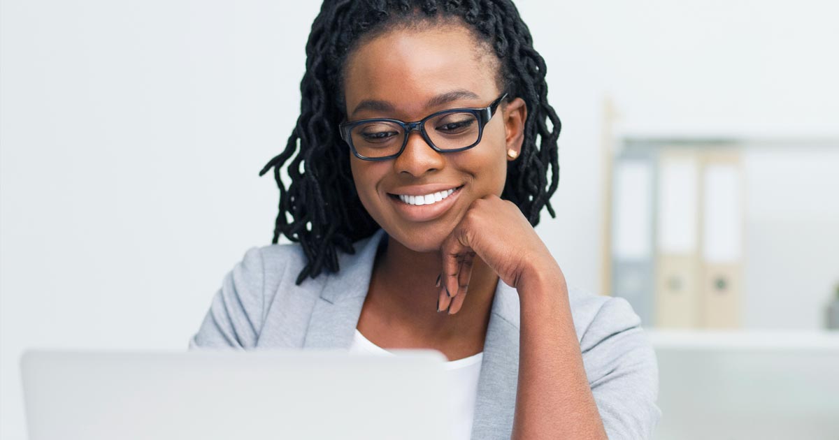 A mental health professional smiles while using her laptop to explore PCOM's MS in Mental Health Counseling grad program