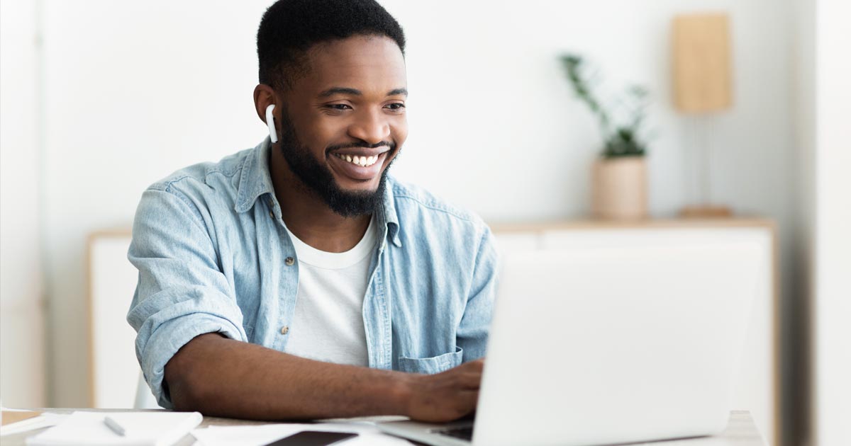 A mental health professional smiles as he uses his laptop to learn about PCOM's MS in Mental Health Counseling program