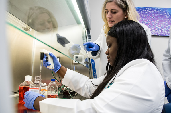 PCOM biomed students smile as they work with liquids in a research lab.