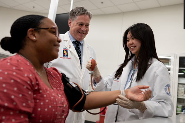 A PCOM Georgia pharmacy student smiles as she takes the blood pressure of a patient alongside a faculty member at PCOM Georgia