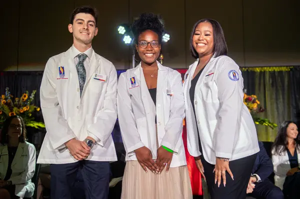 PCOM Georgia pharmacy students smile as they receive white coats on stage from faculty members