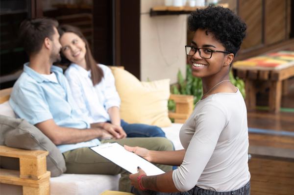 A mental health counselor smiles with her clipboard as she interacts with a couple in an office.