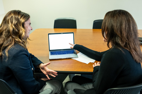 A PCOM school psychology student and faculty member smile as they review online coursework on a laptop