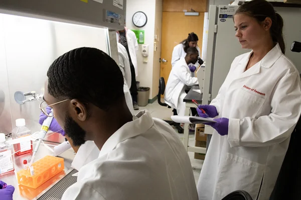 Male student uses lab instrument as female student takes notes.