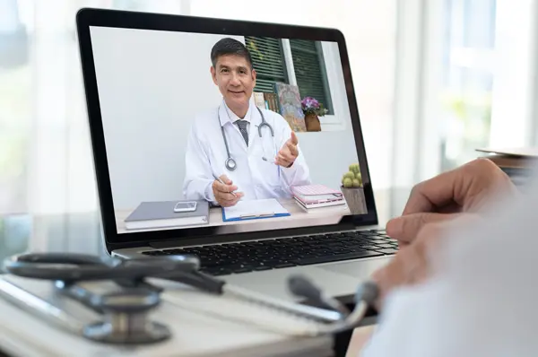 A physician faculty member instructs a medical student via a laptop screen