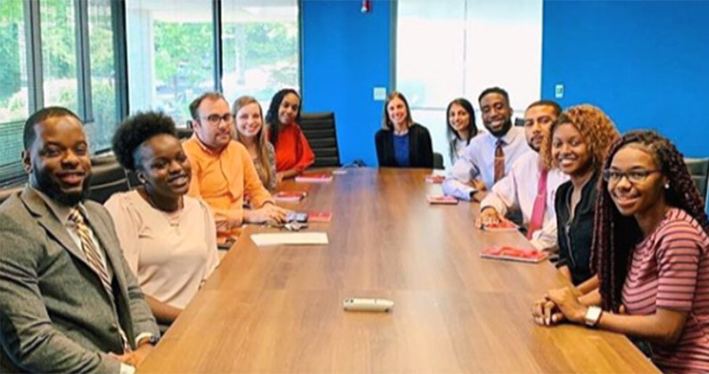 Pharmacy students sit and smile around a conference room table at Encompass RX's office facility.