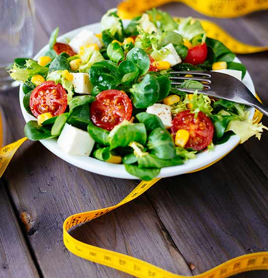 Macro shot of salad, fork and waist tape measure.
