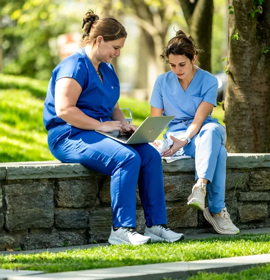 Two med students studying and talking on laptop's outside at PCOM's Philly location