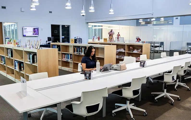 Student sits at long table amid rows of book shelves