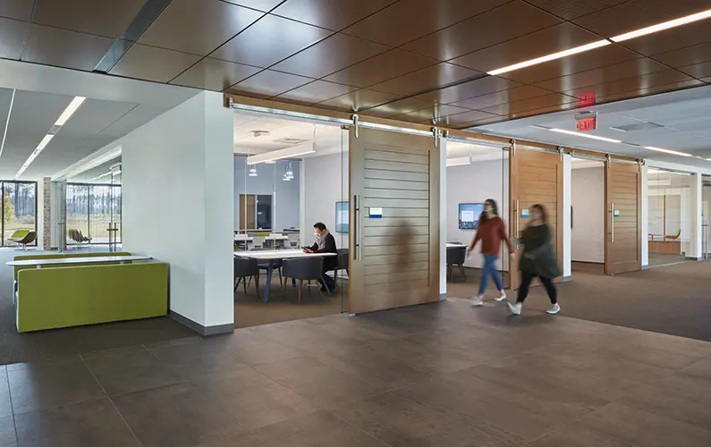 Students walk down wide corridor past individual study spaces separated by oversized sliding doors